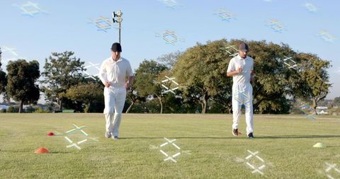 Two cricket players jogging through cone drill on sunny grassy practice pitch for training