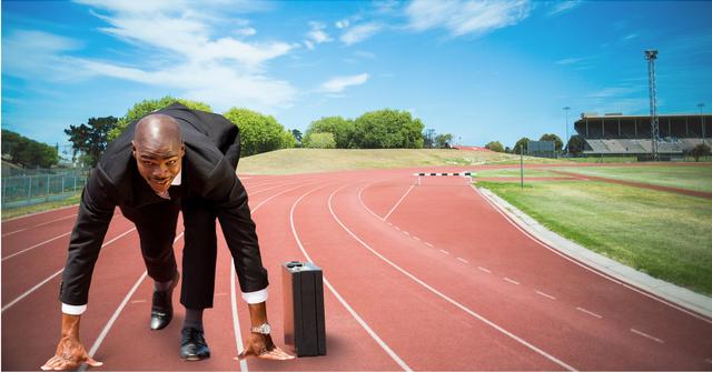 Businessman in suit with briefcase crouching at starting line, ready to race at athletics track. Useful for concepts related to business competition, leadership, determination, and professional challenges.