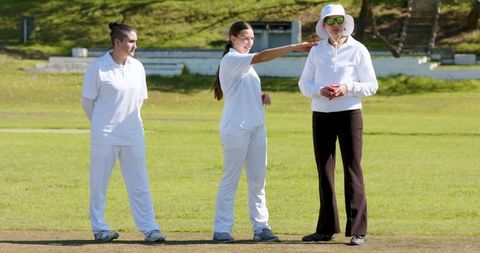 Women cricketers discussing strategy with official on sunny field
