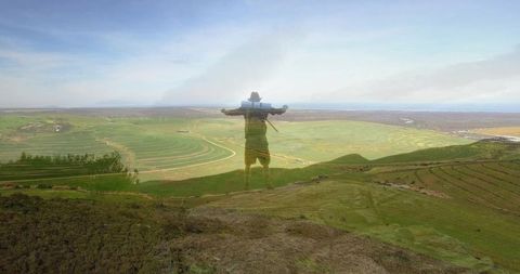 Hiker embracing nature on hilltop overlooking expansive farm fields