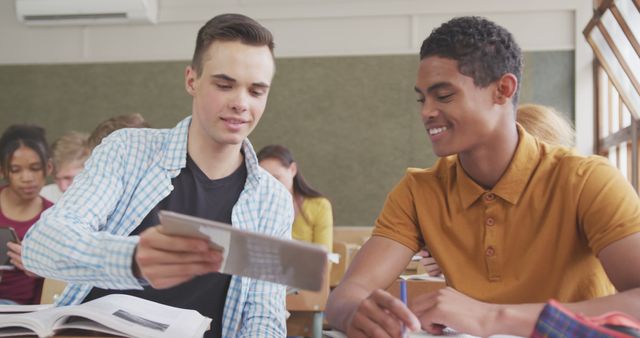 Teenage Caucasian boy and teenage Biracial boy study together at school. They're engaged in a collaborative learning session in a bright classroom.