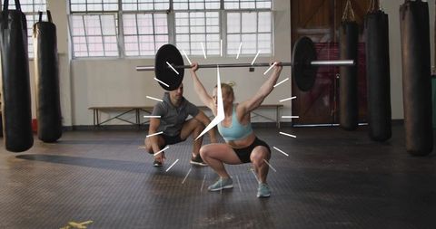 Female athlete performing overhead squat with barbell while trainer spotting in gym clock overlay