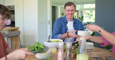 Friends sharing fresh salad around modern dining table, casual home meal and togetherness