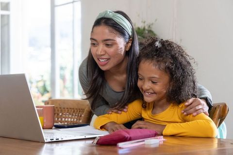 Asian mother tutoring african american daughter at laptop, smiling during remote learning