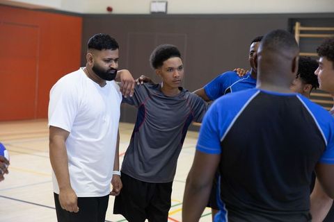 Youth sports team huddling with coach building focus, camaraderie and strategy in gym