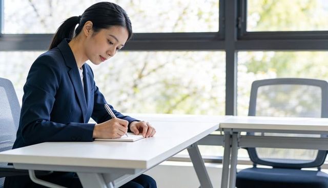 Asian businesswoman writing notes in bright modern office classroom, minimalist workspace