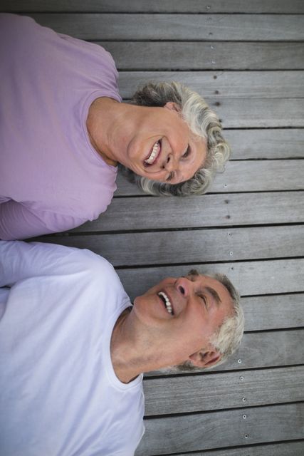 Senior couple lying on wooden porch, smiling and enjoying each other's company. Perfect for themes related to senior lifestyle, retirement, love, and relaxation. Ideal for use in advertisements, brochures, and websites promoting senior living, healthcare, and leisure activities.