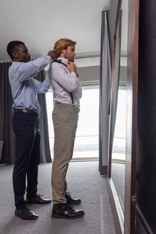 Diverse friends adjusting tie in elegant hotel room with city view