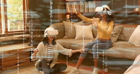 Two women playing virtual reality at home wearing VR headsets reaching digital objects
