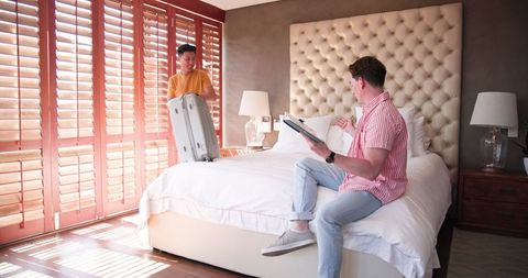 Diverse Couple Packing Suitcase and Enjoying Book in Sunlit Bedroom