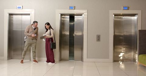 Diverse coworkers collaborating on tablet in modern elevator lobby with walkie talkie