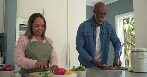 Diverse couple chopping and rinsing fresh vegetables at modern kitchen island, cozy home cooking