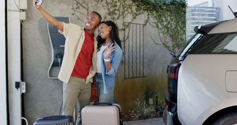 Couple Taking Selfie by Electric Car with Luggage