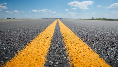 Double yellow center lines leading toward horizon on rural paved road with textured asphalt