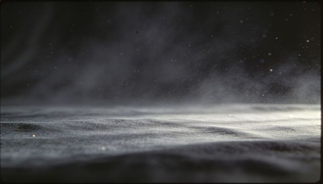 Macro textured dark gray fabric revealing weave and floating dust motes in raking light
