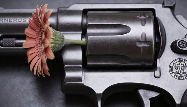 Gerbera stem inserted into revolver cylinder contrasting delicate flower and brushed steel