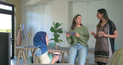 Diverse women coworkers collaborating over coffee and tablet during casual meeting in modern office