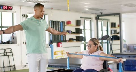 Therapist helping woman with paraplegia in resistance band workout