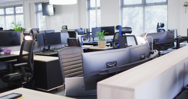 A modern open office space featuring multiple desks equipped with computers, comfortable office chairs, and indoor plants. Ideal for representing business environments, corporate settings, workspace organization, technological setups, and contemporary office design. Perfect for use in articles about remote work return, workplace trends, office setup tips or for illustrating professional work environment concepts.