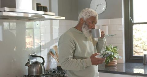 Senior Man Relaxing in Modern Kitchen with Coffee and Smartphone
