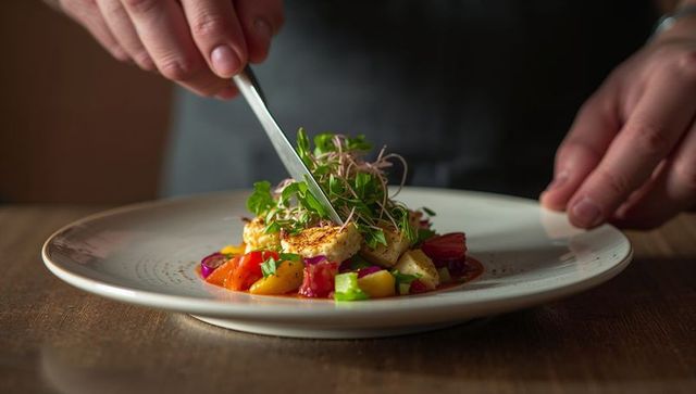 Chef plating seared rounds with microgreens, colorful heirloom vegetables and vibrant sauce