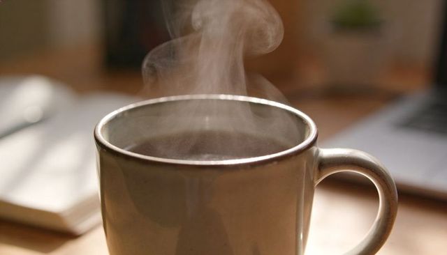 Steaming Beige Ceramic Mug on Wooden Desk with Blurred Notebook and Laptop, Morning Brew