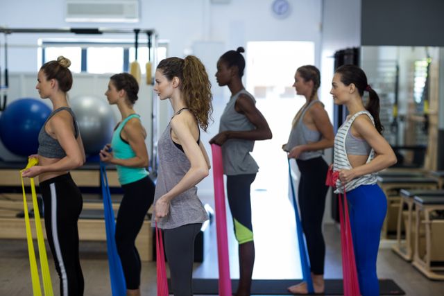 Women are seen exercising with resistance bands in a gym, focusing on stretching and fitness. This image can be used for promoting fitness classes, gym memberships, healthy lifestyle campaigns, or workout equipment. It highlights group exercise and the importance of physical fitness.