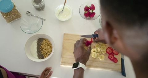 African american couple cutting strawberries for yogurt bowl with granola and banana