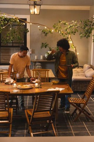 Friends Gathering on Cozy Lit Patio Around Wooden Dining Table for Casual Evening