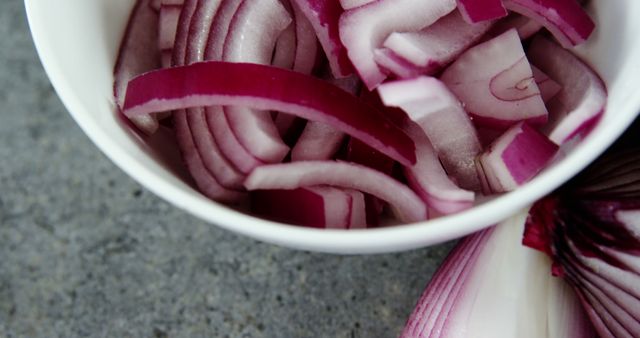 Sliced red onions are arranged in a white bowl, with copy space. Fresh ingredients like these are essential for adding flavor and color to various culinary dishes.
