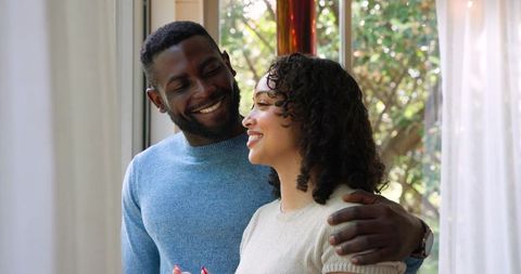Diverse Couple Smiling by Window in Cozy Home