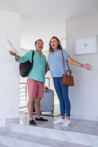 Cheerful Couple Arriving on Vacation at Modern Home with Luggage