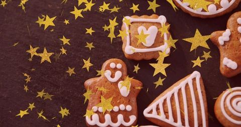 Decorating gingerbread cookies with white icing and gold star confetti on dark slate board