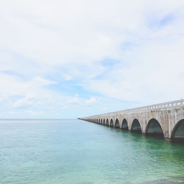 Expansive sea bridge spans calm turquoise ocean water under cloudy skies. Ideal for themes related to travel, transportation, architecture, seascapes, and coastal beauty. Use in advertisements for coastal destinations, engineering marvels, or serene landscapes.