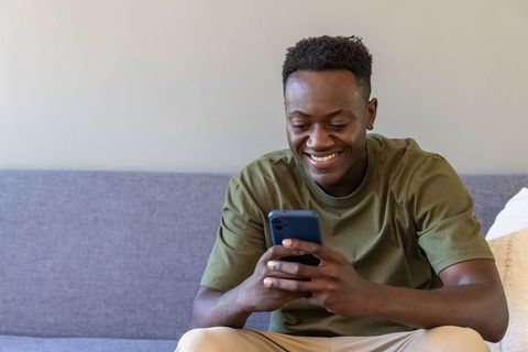 Smiling man sitting on sofa holding smartphone, relaxed home lifestyle