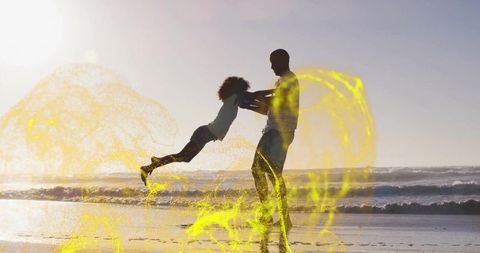 Father swinging daughter on sunlit beach with golden light effects, silhouette joy motion