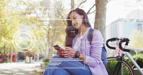 Young woman using smartphone outdoors with bicycle and earbuds in sunny urban park