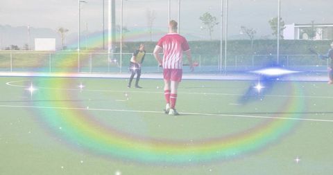 Standing soccer player in red striped kit on fenced turf with rainbow sparkle overlay
