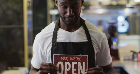 Smiling barista displaying open sign in coffee shop