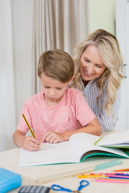 Mother assisting her young son with his homework at home. Ideal for educational content, family-oriented advertisements, parenting blogs, and articles about home learning and parental support in education.