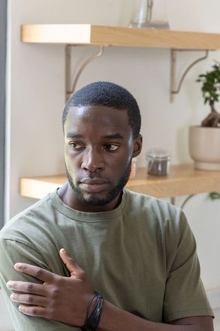 Pensive african american man sitting in minimalist kitchen looking left calm portrait