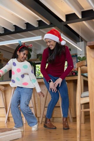 Asian mother and daughter dancing in kitchen wearing santa hat and reindeer antlers