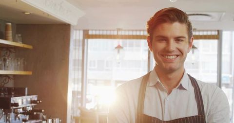 Smiling barista serving espresso behind counter with warm sunlight in urban coffee shop