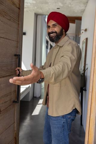 Mid adult indian man opening door and extending hand in welcome gesture