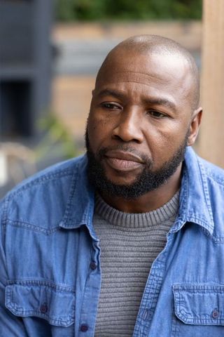 Pensive african american man sitting on deck wearing denim shirt over gray sweater