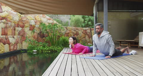 Couple Practicing Yoga on Tranquil Terrace Deck by Water