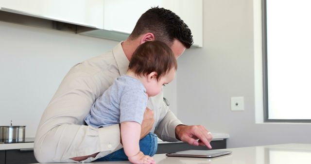 Father holding his baby before work and using tablet at home in the kitchen