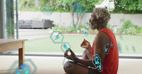 Meditating man practicing mindfulness at home with fitness tracker and teal holographic icons