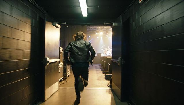 Running musician rushing backstage toward lit stage and drum kit