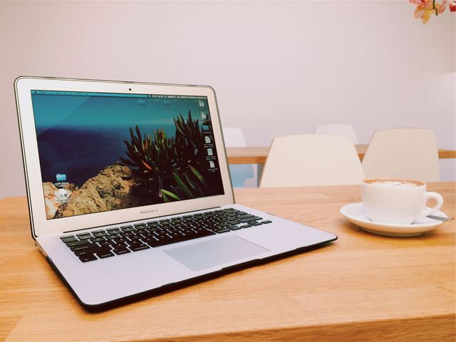 Laptop placed next to a coffee cup on a wooden table in a modern-looking workspace. Ideal for promoting remote work, technology products, or modern office environments. Can be used in blog posts about productivity, work-life balance, or home offices.